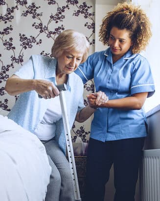 aide assisting elderly woman in getting up from bed
